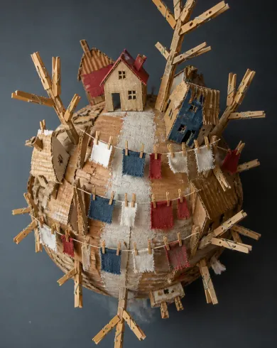 手工紙藝／立體拼貼作品，描繪瓦楞紙小行星被曬衣繩、布片、房屋與衣夾樹環繞。直式構圖保留清晰主體、自然材質與光線細節。