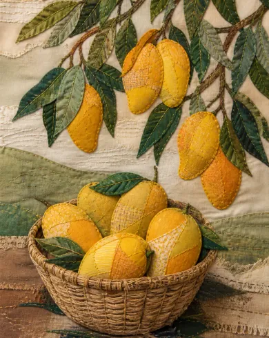 手工刺繡與布貼／舊棉布作品，描繪大小芒果、葉片與果籃以黃色布貼和綠色縫線組成。直式構圖保留清楚主體與真實工藝材質。