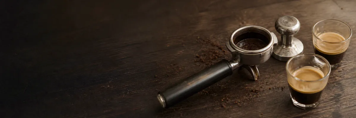 Portafilter, tamper and two espresso shots with hazelnut crema on a dark wooden table