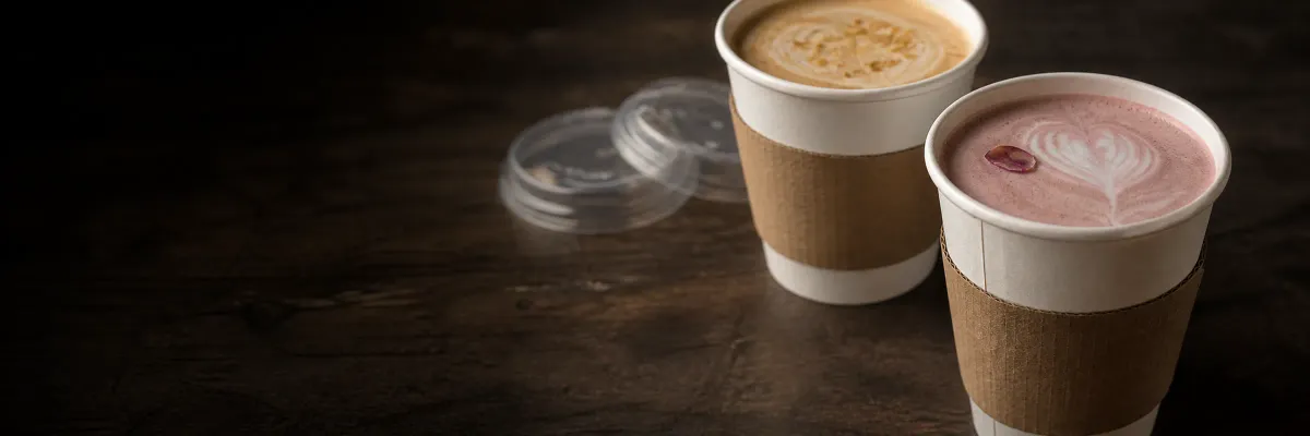 Two seasonal hot drinks on dark wood, one pink with latte art and one topped with golden spice